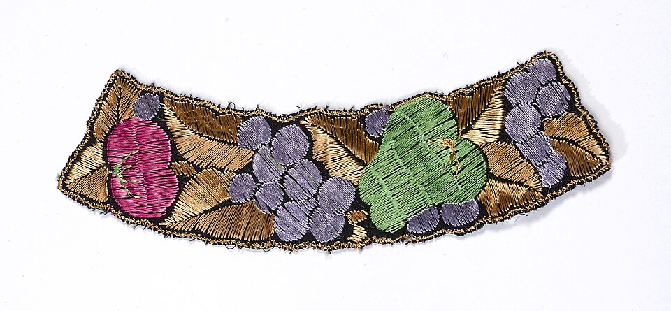 Appliqué fabric patch — embroidered fruit cluster with pink peach, green pear, and purple grapes, outlined in gold stitching on cream fabric