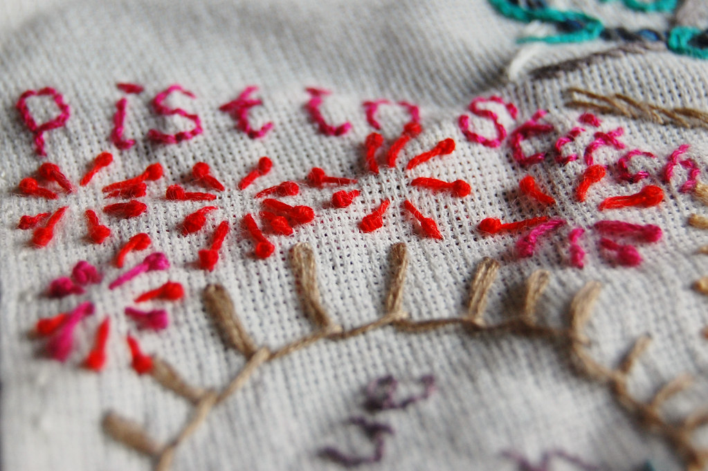 Close-up of embroidery needle and colourful thread stitching a floral pattern on linen fabric